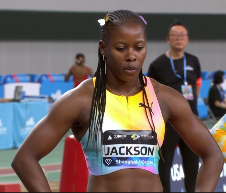 Jamaica's Shericka Jackson standing on a track, wearing a colorful gradient sleeveless top and bib reading 'JACKSON' for Shangha Diamond League focused before a race.